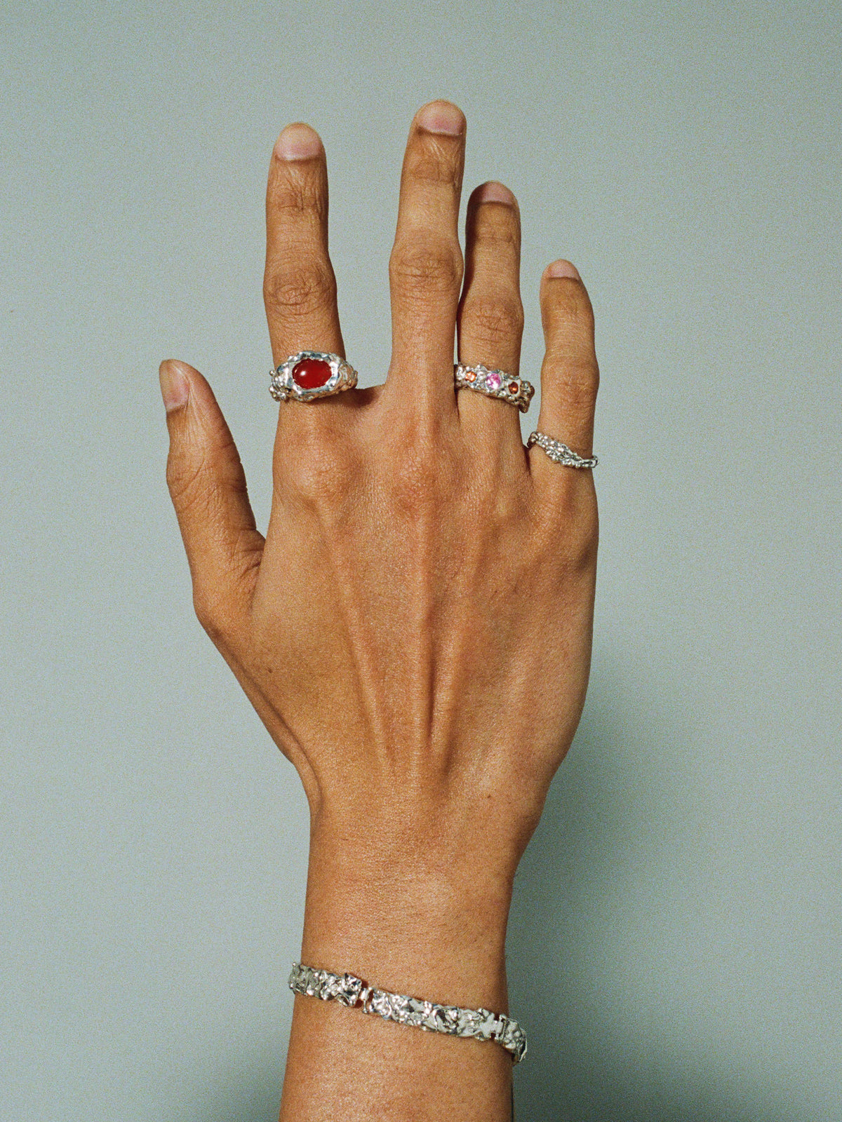 FARIS ROCA WAVE Ring in sterling silver worn on model. Styled with ROCA EYE Ring in silver with carnelian, ROCA GEM Band in sterling silver with lab-created pink and orange sapphire, and BRUTO Bracelet.