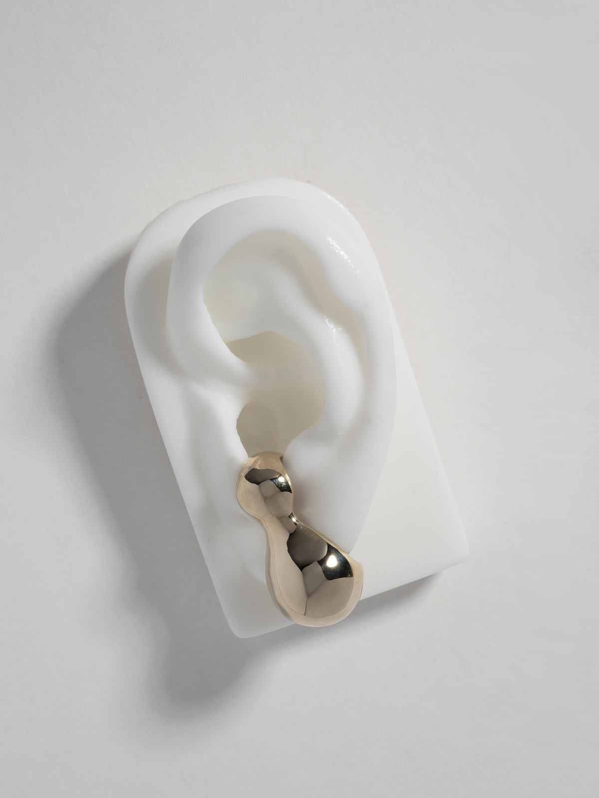 Close up product image of FARIS BOLO Stud in gold-plated bronze, shown on white silicone ear display.