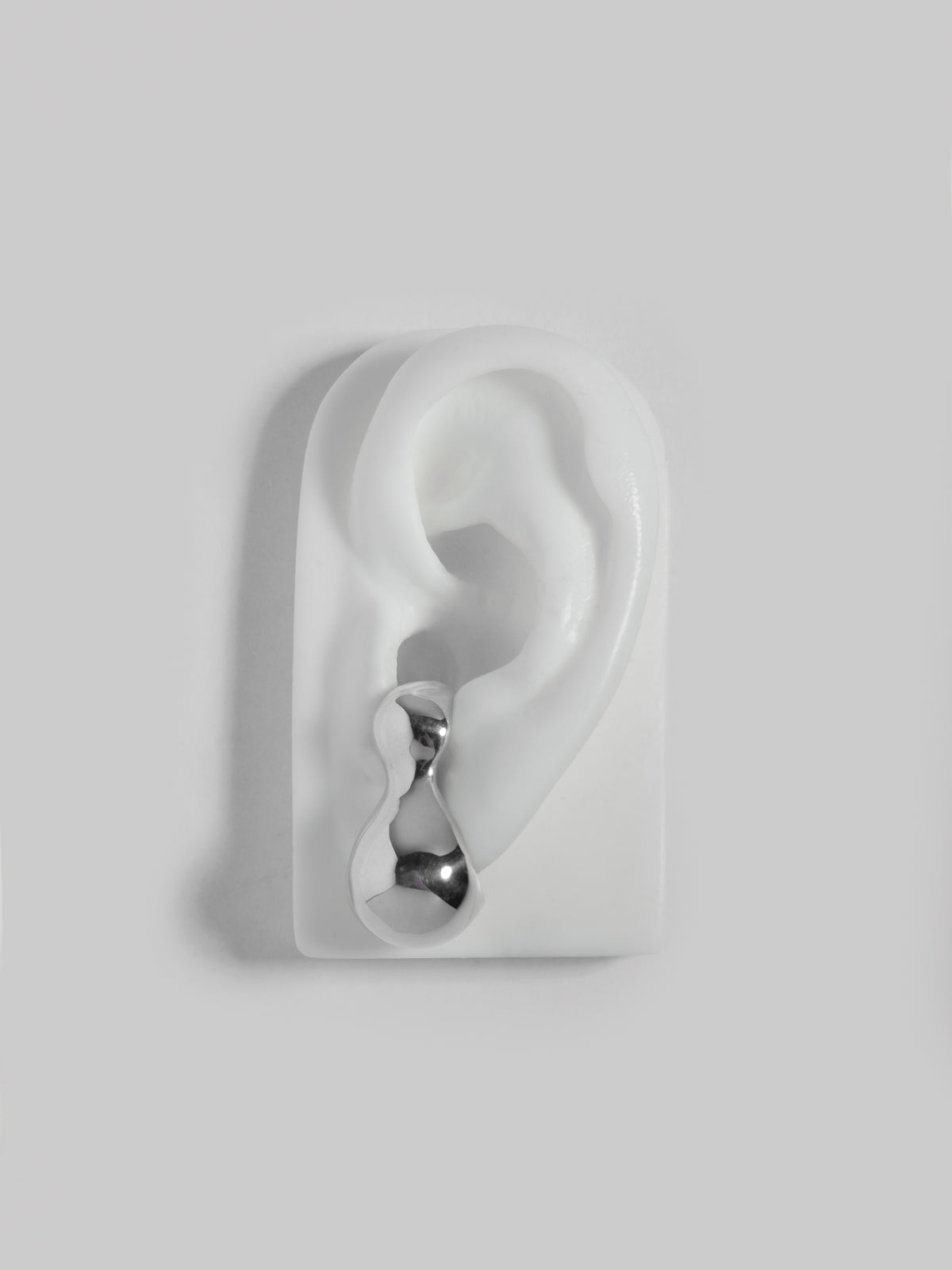 Close up product image of FARIS BOLO Stud in sterling silver, shown on white silicone ear display (front view)