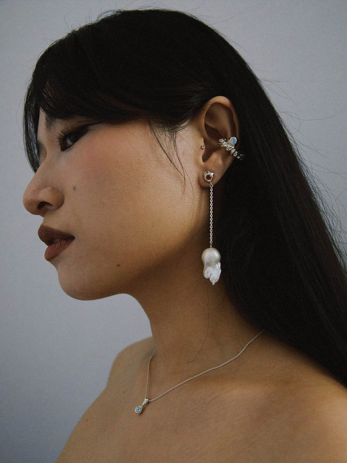 FARIS VENUS Drops in sterling silver with lab-created orange sapphire shown on model. Styled with ROCA GEM Ear Cuff in sterling silver with topaz, and BOLITO Necklace in sterling silver with topaz. Long side of asymmetrical earring shown