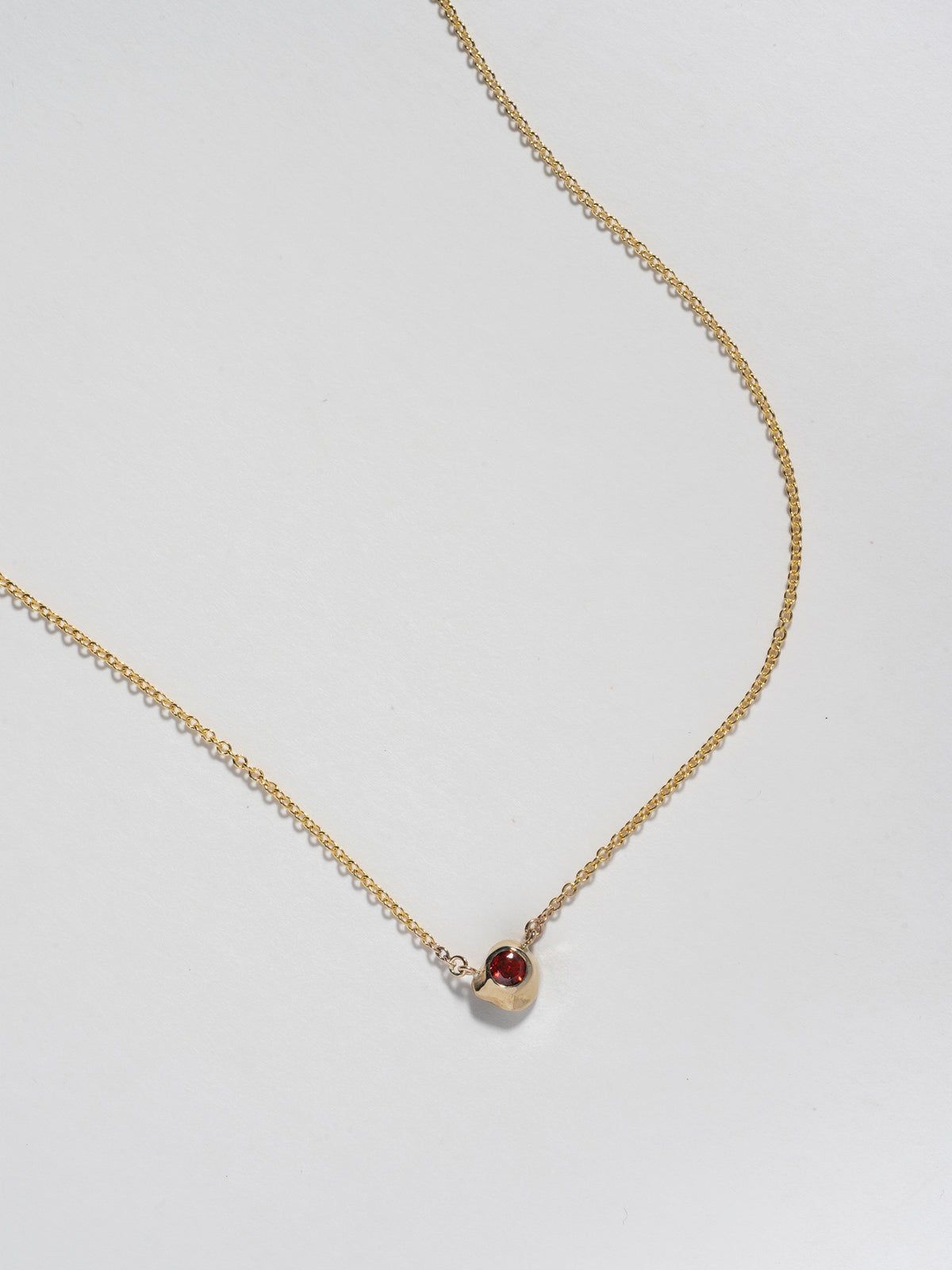 Close up image of FARIS KIRA Necklace pendant in 14k gold with garnet