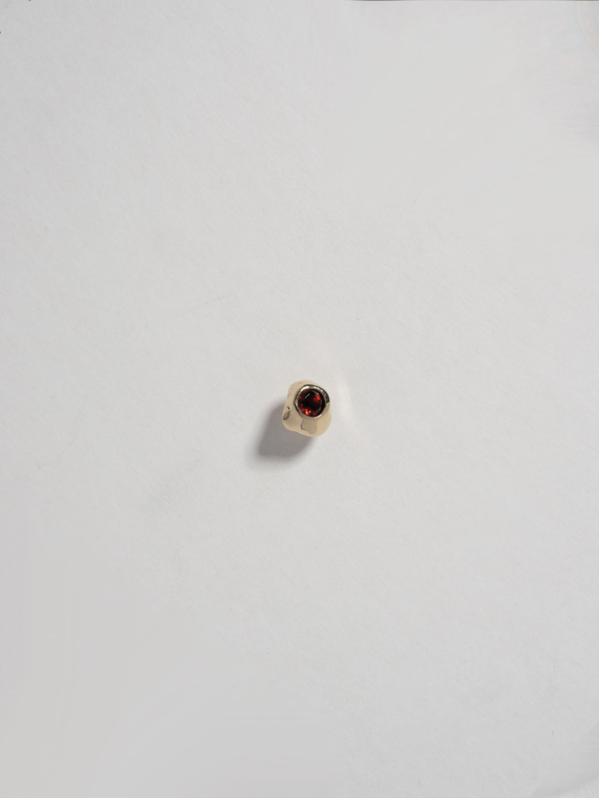 Close up product image of FARIS KIRA Stud in 14k gold with garnet, shown on white background (front view)