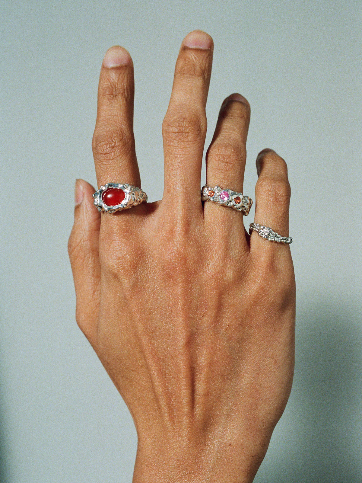FARIS ROCA GEM Band in sterling silver with lab-created pink and orange sapphire worn on model. Styled with ROCA EYE Ring in silver with carnelian, and ROCA WAVE Ring in silver