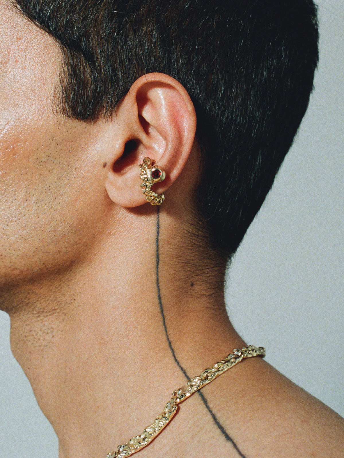 FARIS ROCA GEM Ear Cuff in gold-plated bronze with garnet worn on male model. Styled with BRUTO Collar in gold-plated bronze