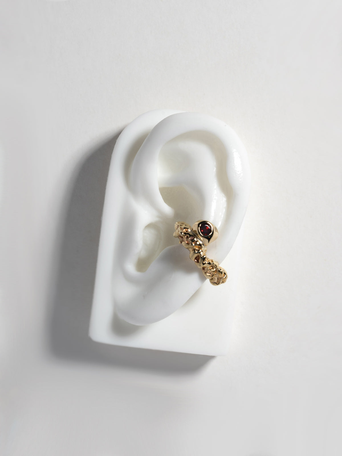 Product image of FARIS ROCA GEM Ear Cuff in gold-plated bronze with garnet, shown on white, silicone ear display