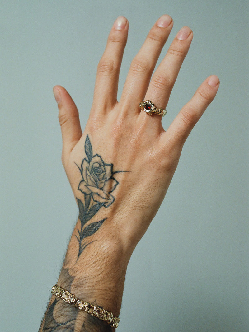 FARIS BRUTO Bracelet in Gold-Plated Bronze shown on male model with flower tattoo on face of hand. Styled with SPELL Ring in Gold-Plated Bronze with Garnet.