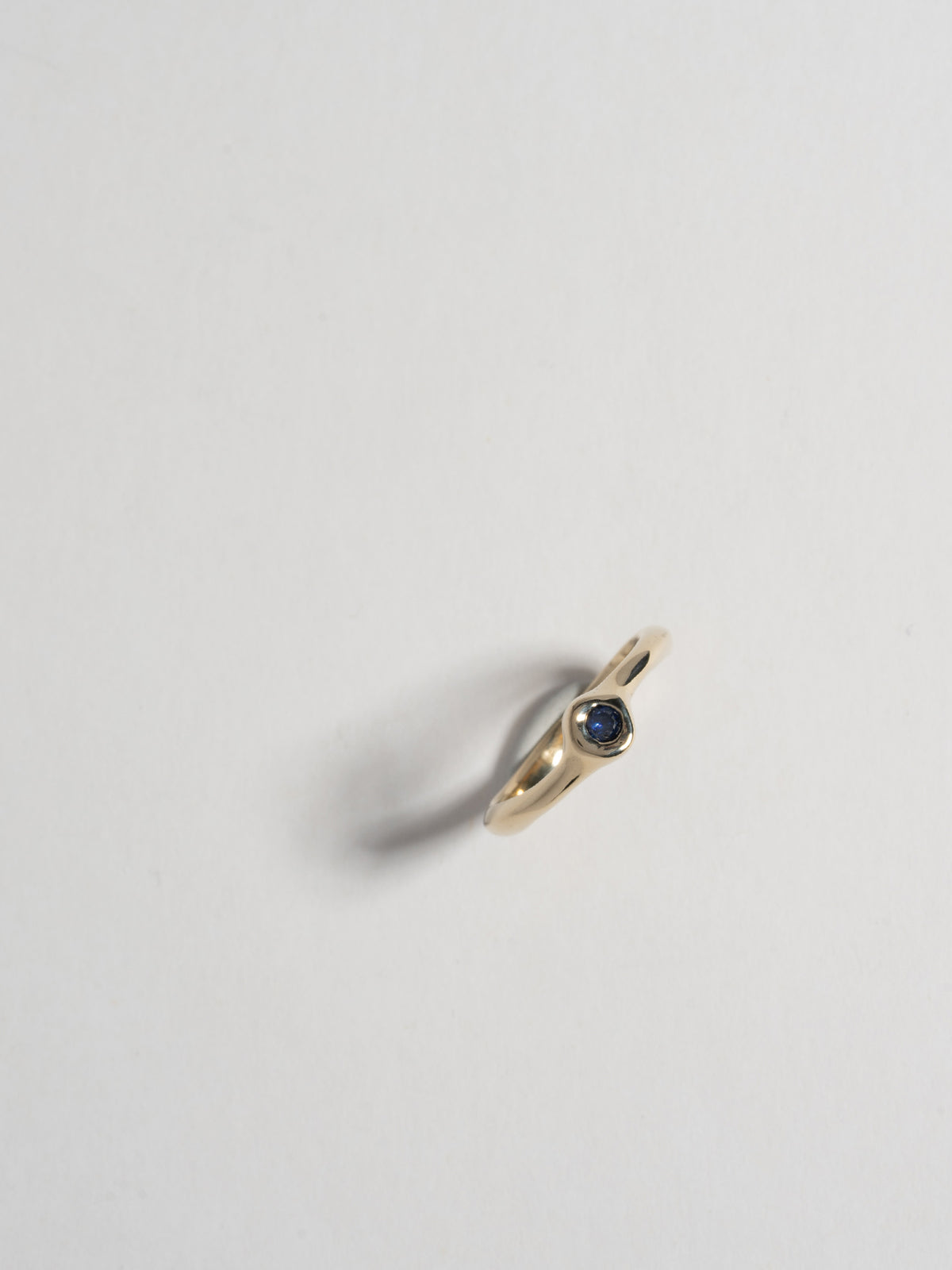 Close up image of FARIS SUGAR Ring in 14k gold with blue sapphire, standing up-right on white background. Front view