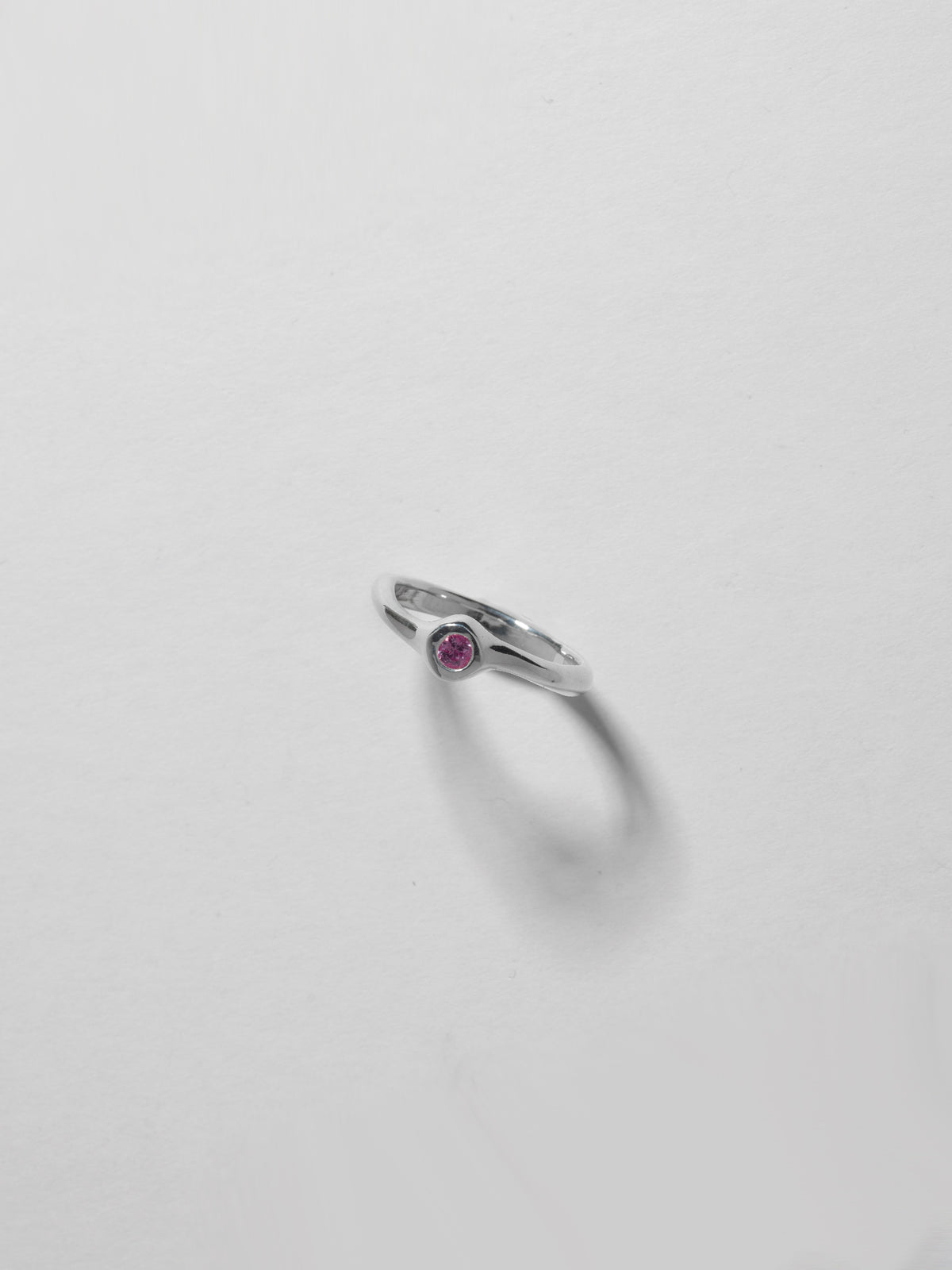 Close up image of FARIS SUGAR Ring in sterling silver with pink sapphire, standing up-right on white background, front view, gem visible