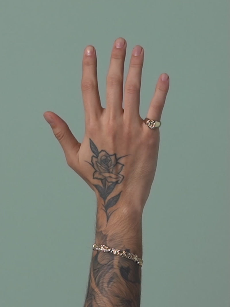 Short clip of FARIS BRUTO Bracelet in gold-plated bronze shown on male model with tattoo sleeve. Styled with ROCA CROWN Signet ring in gold-plated bronze, worn on model's pinky finger. Rose tattoo on face of models hand
