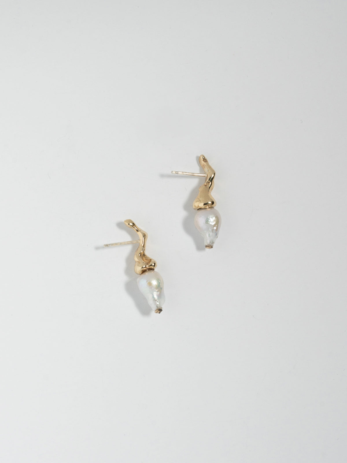 Product image of FARIS SPRIG PERLA in 14k gold. The pair of earrings are laid on its side, showing the post and earrings asymmetrical profile